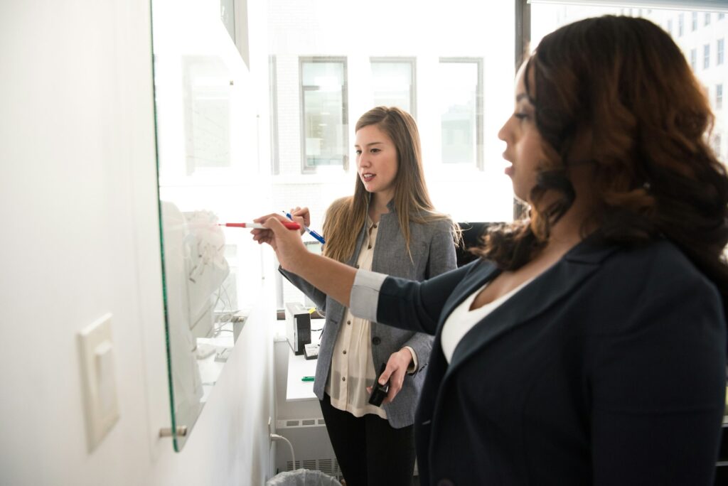 two professional women write on whiteboard